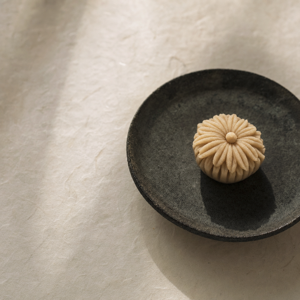 A single chrysanthemum-shaped wagashi sweet on a dark ceramic plate